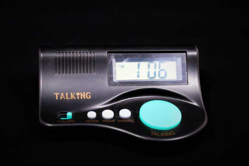 A clock with digital display, speaker, three small buttons and one large button.